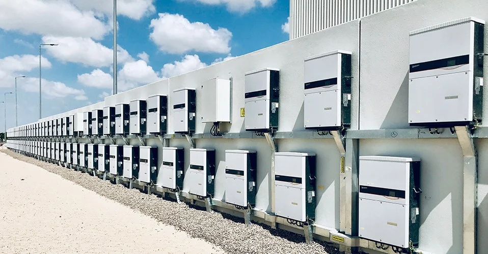 A close-up of a modern solar inverter with digital monitoring lights against a blurred grid background.