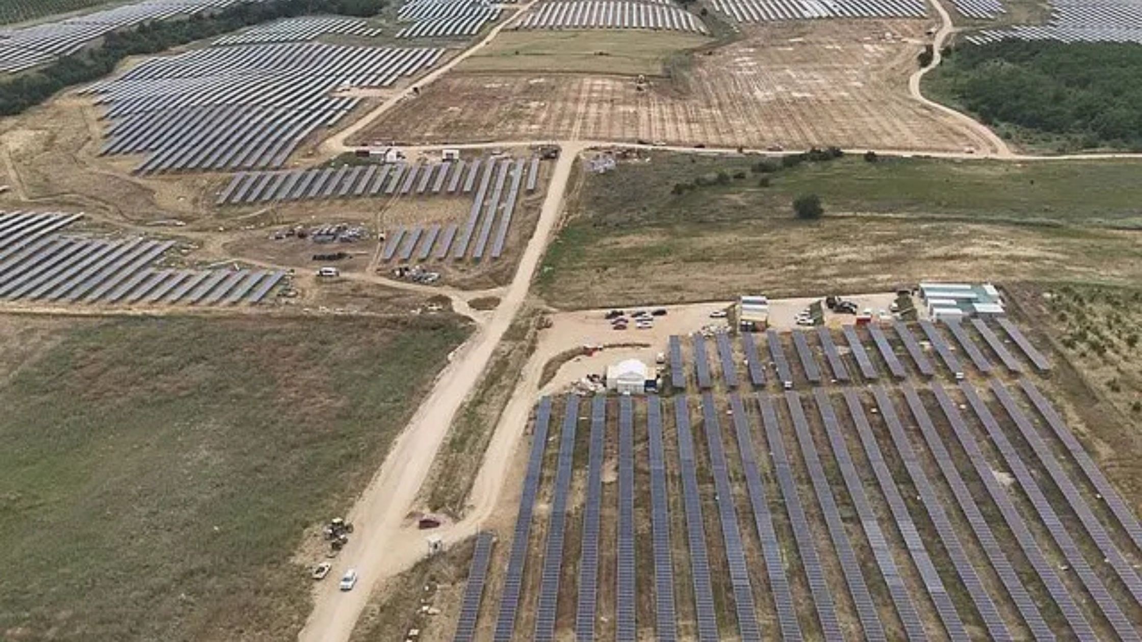 Large scale solar farm construction site with rows of photovoltaic panels and cranes