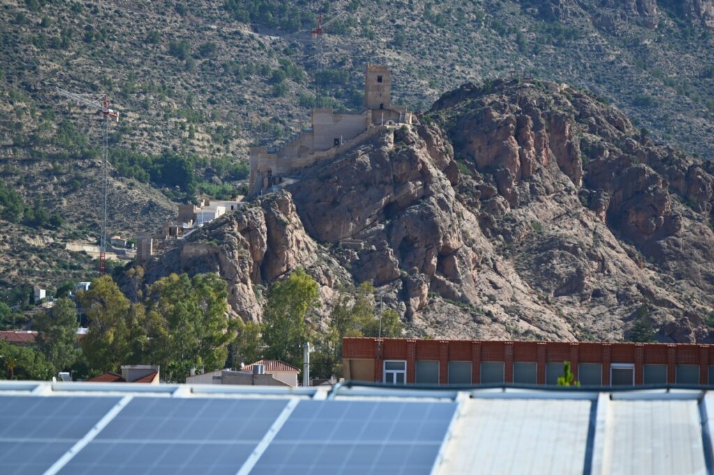 Workers installing solar thermal collectors and PV panels on a municipal building roof in Spain.