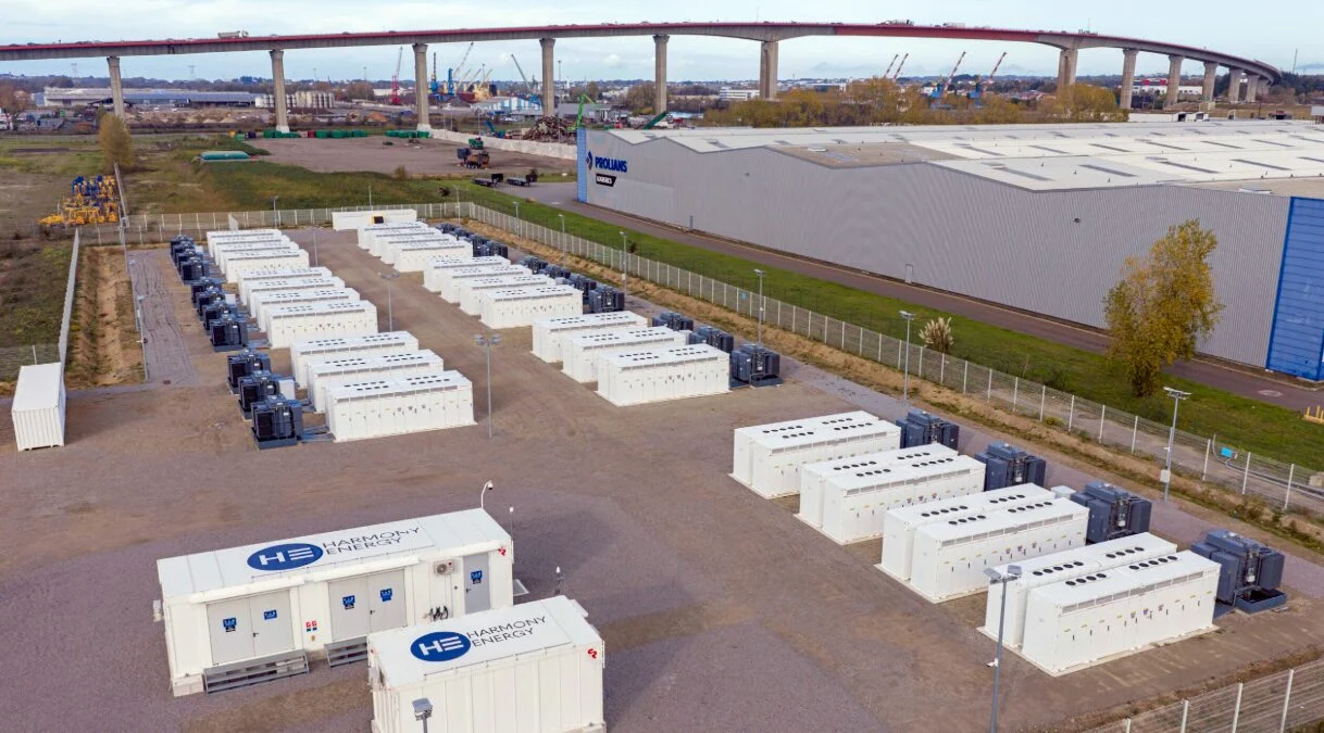 Large scale battery energy storage system containers in a field with power lines in the background.