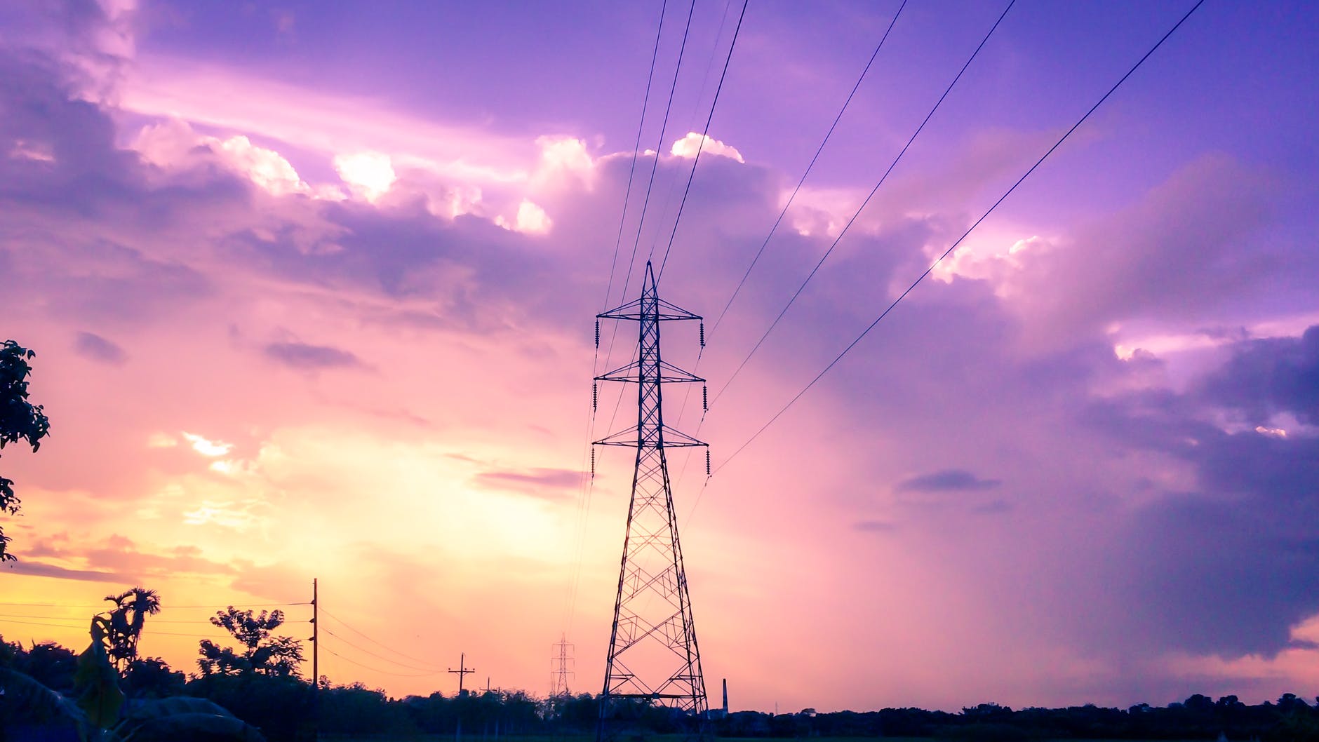 Electric power transmission towers set against a sunset sky representing renewable energy transition.