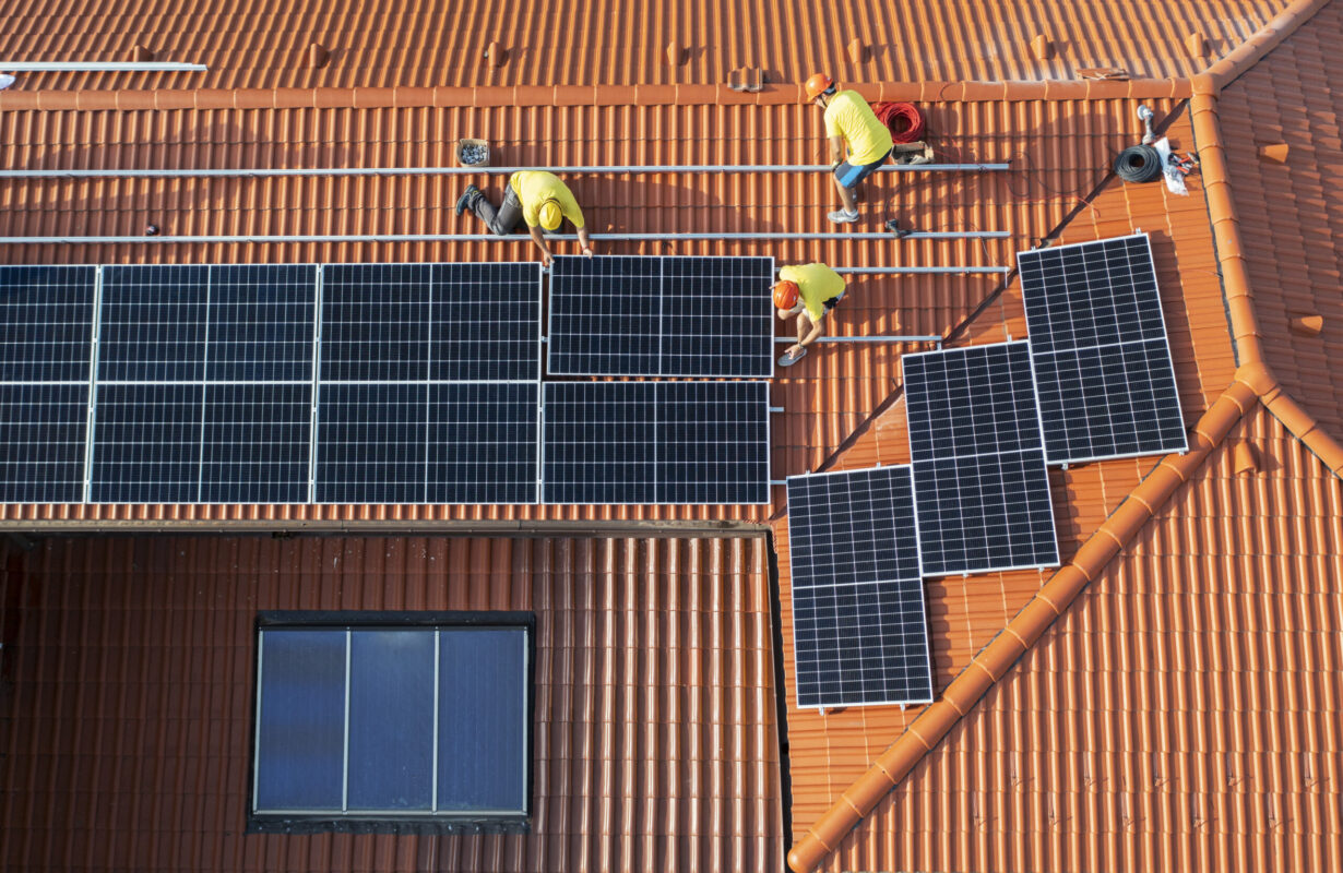 A modern residential home equipped with rooftop solar panels and a battery storage system unit.
