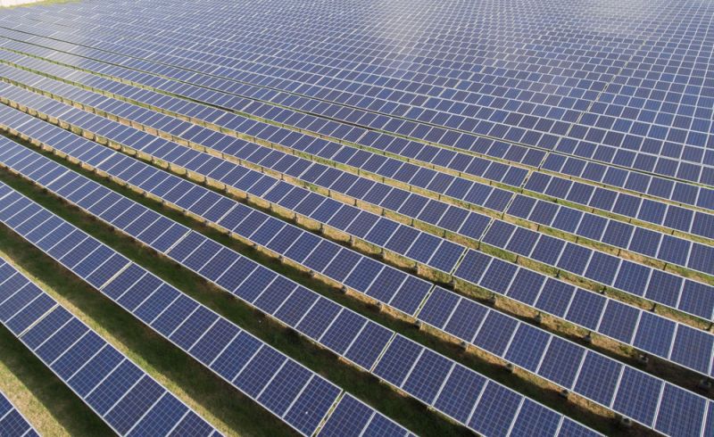 A large-scale solar farm layout with battery storage containers in an open field.