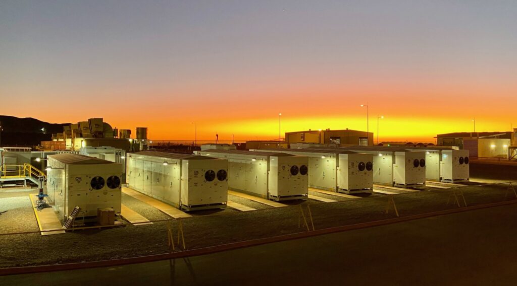Large scale industrial battery storage containers in a field next to a solar farm